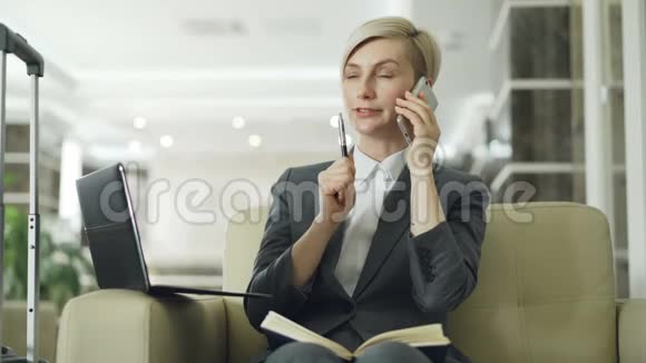 金发忙碌的女商人坐在酒店大堂的扶手椅上在笔记本电脑里写字视频的预览图