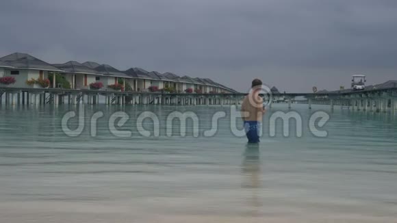 一个人走进海洋站在水上别墅前马尔代夫的白色沙滩视频的预览图
