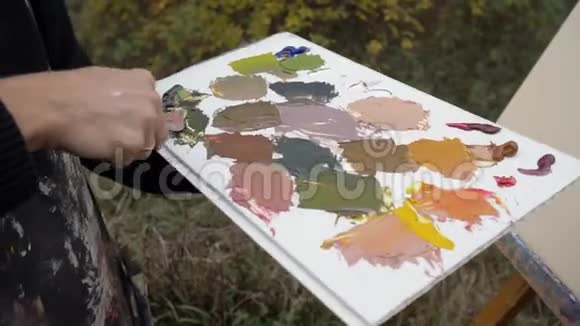 艺术家调色板刀油画在调色板上混合色彩手持特写艺术家在河边的街道上4K视频的预览图