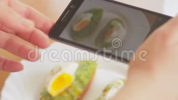 餐馆里的一个女人用手机摄像头拍下食物的照片三明治和荷包鸡蛋和鳄梨视频的预览图