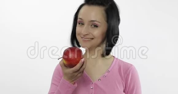 年轻漂亮的女人在白色的背景下吃着又大又鲜又多汁的红苹果视频的预览图