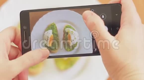 餐馆里的一个女人用手机摄像头拍下食物的照片三明治和荷包鸡蛋和鳄梨视频的预览图