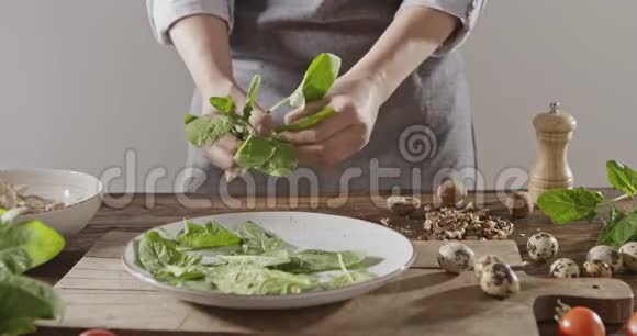 一个穿围裙的女人把菠菜叶子扔到白色的陶瓷盘子里背景有鹌鹑蛋鸡柳青菜视频的预览图