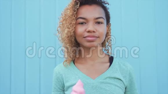 年轻的非洲女孩在蓝墙背景下吃粉色融化冰淇淋视频的预览图