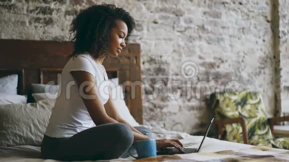 快乐的混血女孩在笔记本电脑上打字分享坐在家里的社交媒体视频的预览图