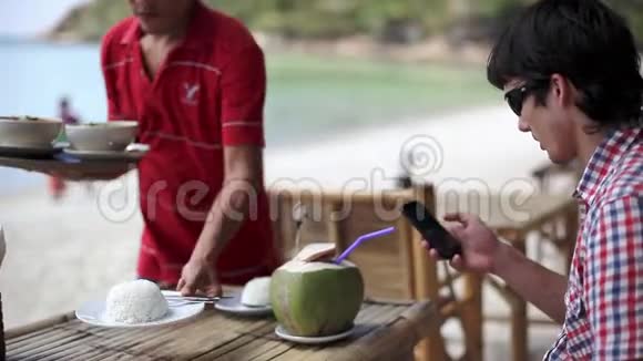 戴太阳镜的帅哥在海滩咖啡馆喝新鲜的椰子汁服务员带汤姆来的时候用手机视频的预览图