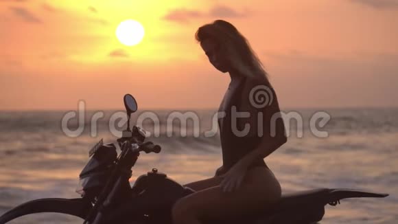 模特穿着黑色比基尼在海边的摩托车上摆姿势一个身材苗条的女孩骑着自行车的轮廓视频的预览图