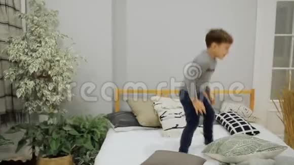 5岁到7岁的男孩穿着蓝色牛仔裤和灰色毛衣在父母的床上高兴地跳起来视频的预览图