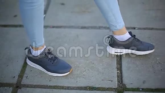 在城市沥青的背景下穿着牛仔裤和运动鞋跳舞的女孩的腿视频的预览图