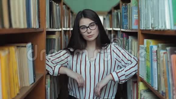 图书馆里年轻漂亮女孩的肖像女学生在书架之间的许多书中学习视频的预览图