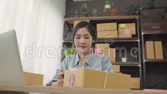 美丽的亚洲年轻企业家女企业家中小企业检查产品的股票扫描QR代码在家工作视频的预览图
