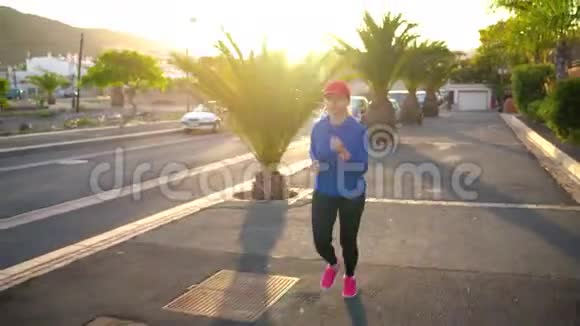 日落时分女人沿着街道在棕榈树之间奔跑健康的生活方式视频的预览图
