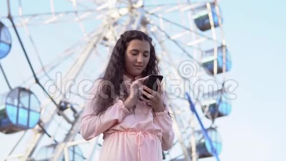 女孩用手机站在摩天轮附近慢动作视频的预览图