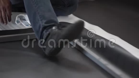 穿着黑色鞋子和深色牛仔裤的男人踩着黑色的床单和灰色的金属框架视频的预览图