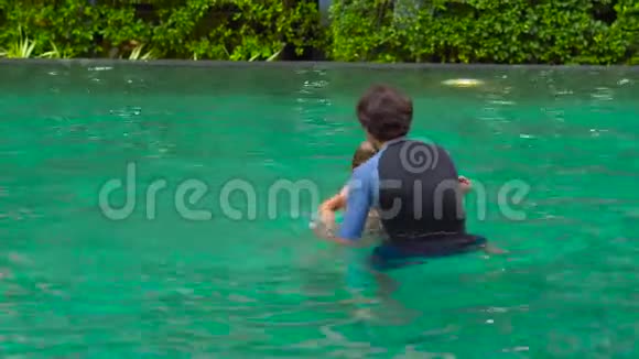 快乐的父子在游泳池里玩耍父亲把儿子扔进水里让他在掉进水里之前翻筋斗视频的预览图