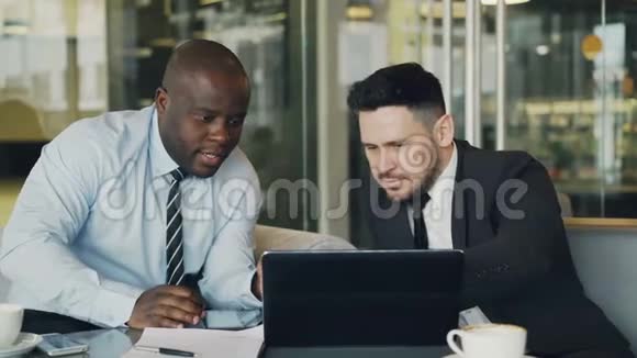 两位商务同事正在看手提电脑并在玻璃墙的现代办公室讨论他们的项目视频的预览图
