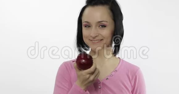 年轻漂亮的女人在白色的背景下吃着又大又鲜又多汁的红苹果视频的预览图