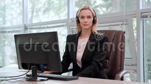 一个穿着黑色夹克的年轻漂亮的女人坐在办公桌前的行政椅上等等视频的预览图