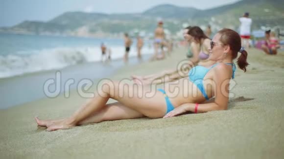 一个穿蓝色泳衣的女人躺在海滩上戴着太阳镜的布鲁内特躺在海里视频的预览图