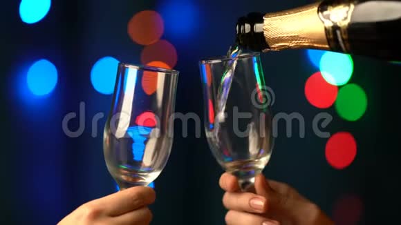在模糊的背景下人们用两杯香槟在闪烁着五彩斑斓的圣诞灯上斟满香槟视频的预览图