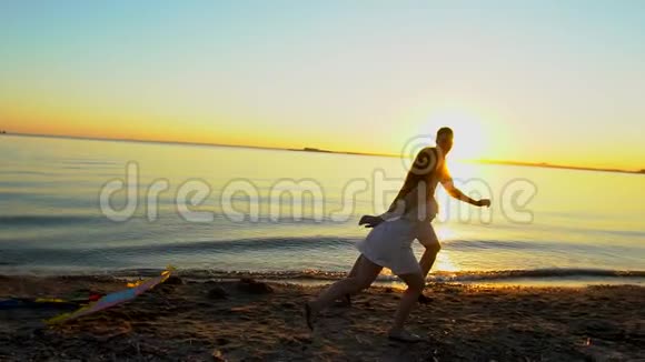 年轻的幸福夫妇在日落时在海边玩风筝男人和女人在阳光下享受时光视频的预览图