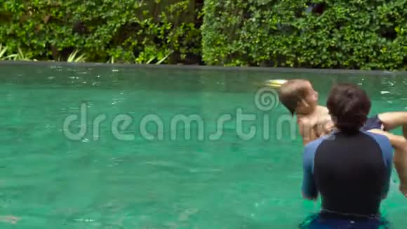 快乐的父子在游泳池里玩耍父亲把儿子扔进水里让他在掉进水里之前翻筋斗视频的预览图