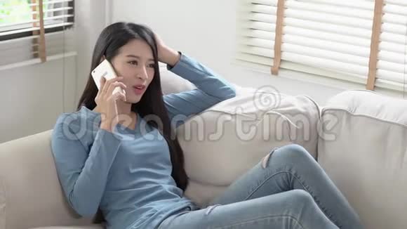 美丽的年轻亚洲女人微笑着躺在沙发上放松女孩坐在沙发上用手机聊天享受视频的预览图