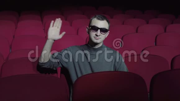 一个单身男人坐在黑色电影院里舒适的红椅子上挥舞着手拿相机视频的预览图