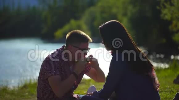 年轻人和女人在河边的森林里野餐吃西瓜背景是山4千克视频的预览图