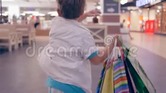 在时尚精品店购物后一个手拿着包裹的购物者会穿过购物中心视频的预览图