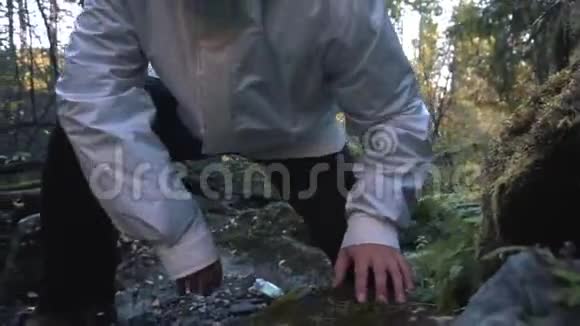 穿着白色夹克和橡胶靴的年轻人在美丽的秋天森林里爬大石头录像特写视频的预览图