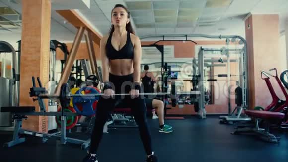 年轻漂亮的女孩长发在健身房做运动用杠铃在蹲4千克视频的预览图
