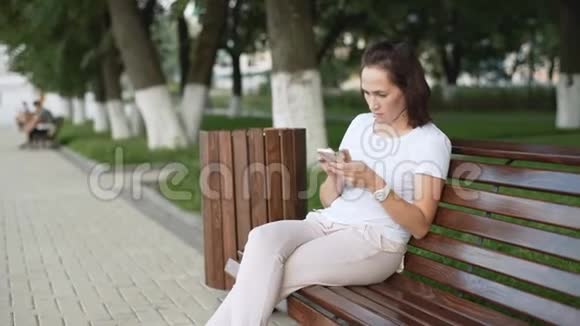 在城市公园里用智能手机很开心一位坐在城市公园长椅上的女士正在收到一条短信视频的预览图
