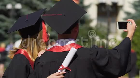 一男一女穿着学术礼服和帽子在毕业典礼上自拍视频的预览图