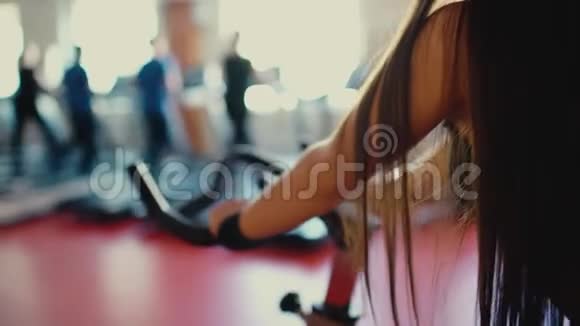 一个头发长长的漂亮黑发女孩骑着自行车在健身房背景4k视频的预览图