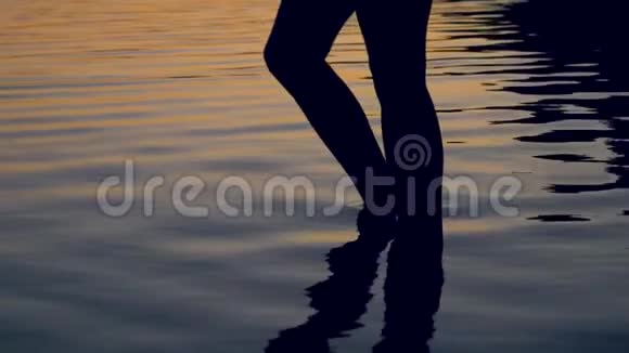 女腿的剪影优雅地在夕阳下的湖中向膝盖深处走去视频的预览图
