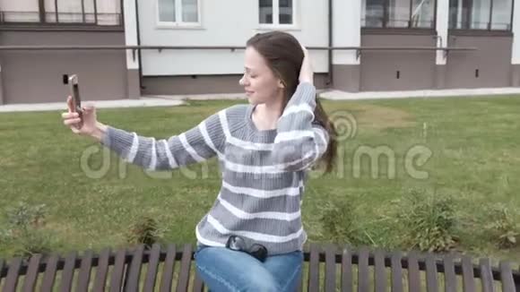 美丽的黑发女人正试图在风中在手机上自拍而坐在长凳上视频的预览图