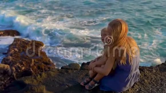 一对母亲和儿子坐在岩石上看着塔纳罗得寺附近的海浪慢镜头视频的预览图