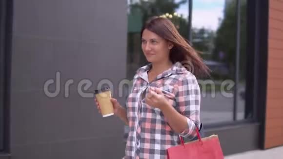 一个穿裙子的漂亮女孩带着包裹去购物手里拿着一杯咖啡慢动作视频的预览图