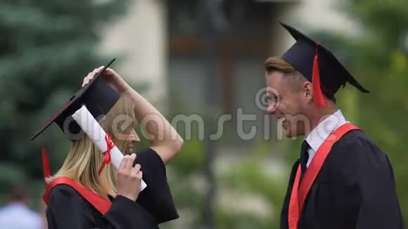 穿着学术服装的漂亮女士拥抱男友微笑毕业派对视频的预览图