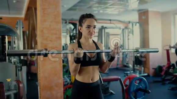 年轻的运动女性深色头发在健身房里提着杠铃棒4千克视频的预览图