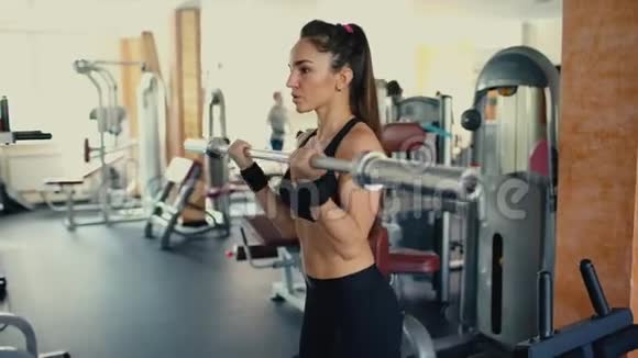 年轻的运动女性深色头发在健身房里提着杠铃棒4千克视频的预览图