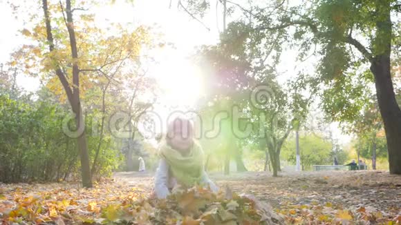 背光的小女孩在户外玩得很开心在秋天公园慢动作地扔黄叶视频的预览图
