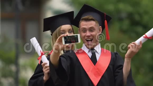 微笑男女毕业生在智能手机上拍摄视频玩得开心视频的预览图