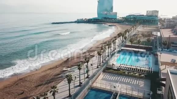 鸟瞰美丽的海岸线现代建筑游泳池和人们在蓝天的海滩上散步视频的预览图