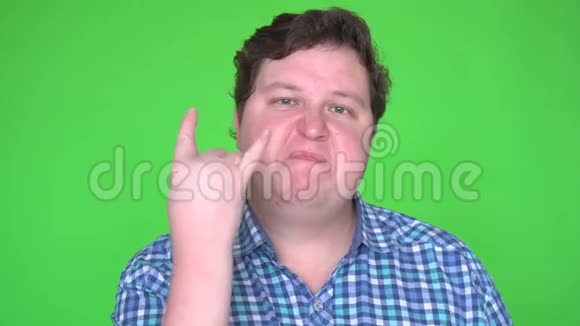 胖子摇滚歌手的肖像用手打手势在绿色背景下看着相机视频的预览图