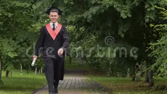 快乐微笑的毕业生带着毕业证书在公园散步兴奋地跳跃着视频的预览图