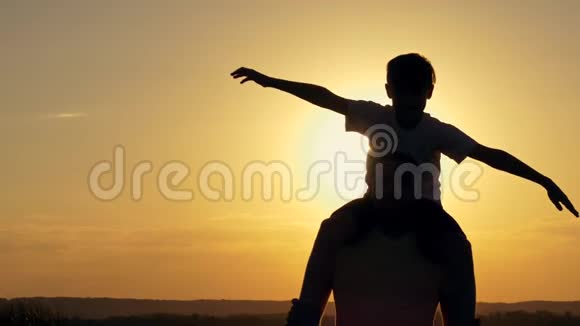 一个幸福的家庭父亲肩上男孩正在玩飞机玩具日落时在湖边剪影视频的预览图