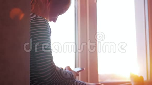 一个小女孩在日落的背景下在窗台上打开的窗户上用书想象故事儿童读物视频的预览图