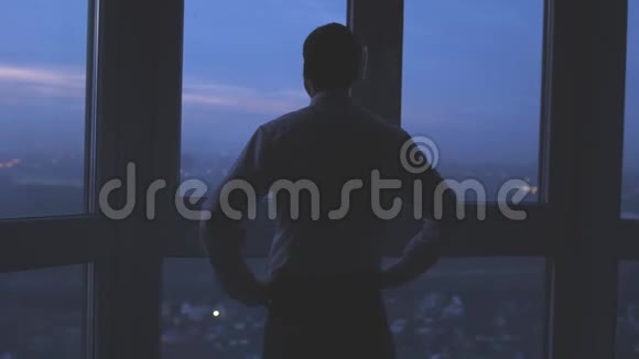 商人的后景站在窗户附近看着夜晚的城市背景3840x2160视频的预览图
